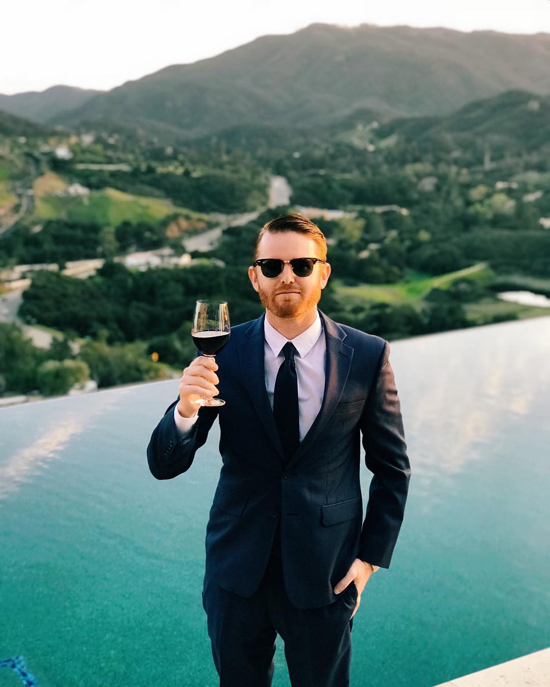 Patrick Bushe in a navy suit holding a glass of red wine in Malibu