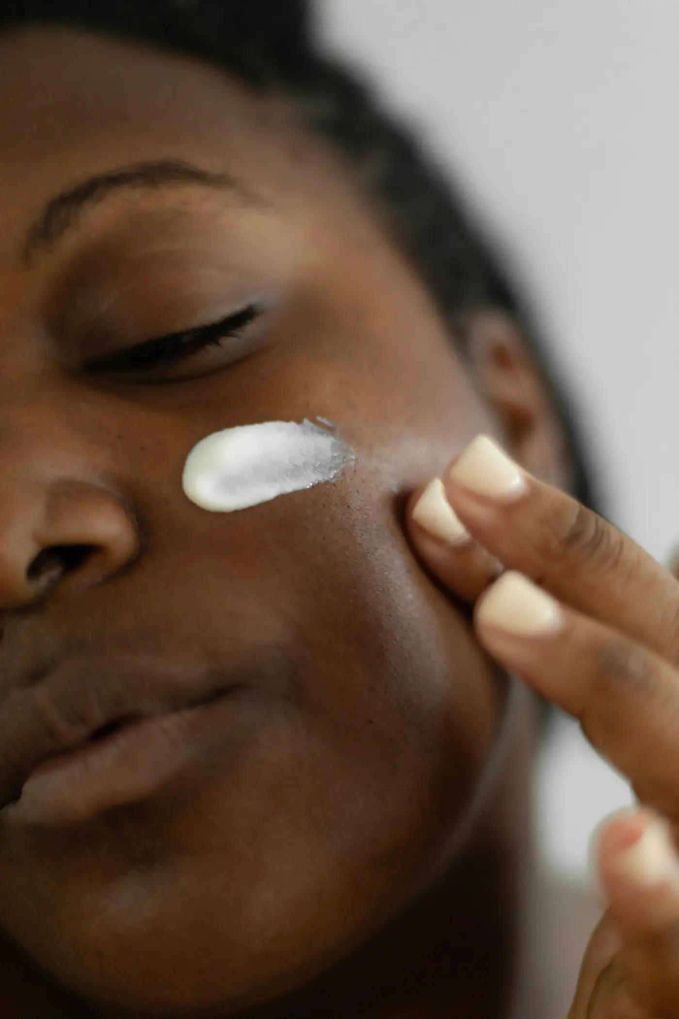 A woman dabbing white cream onto her cheek