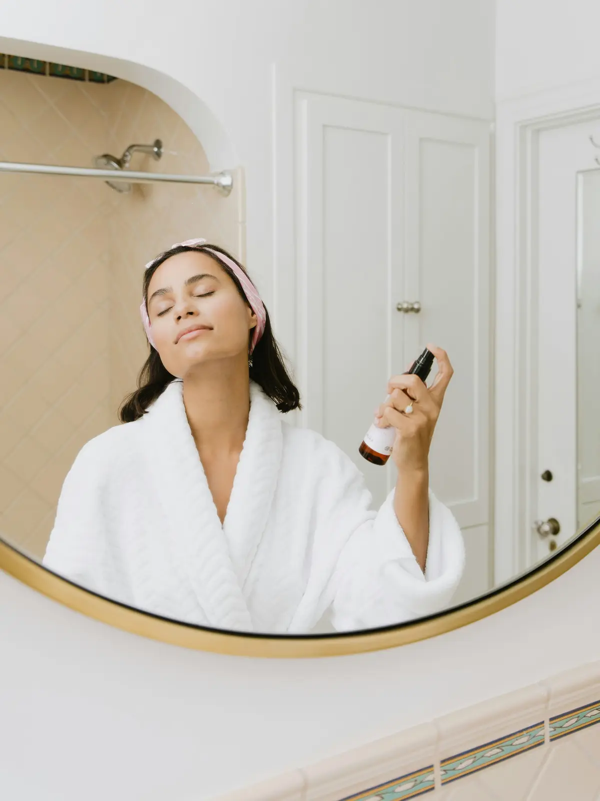 A woman in a robe doing her skincare in a round mirror