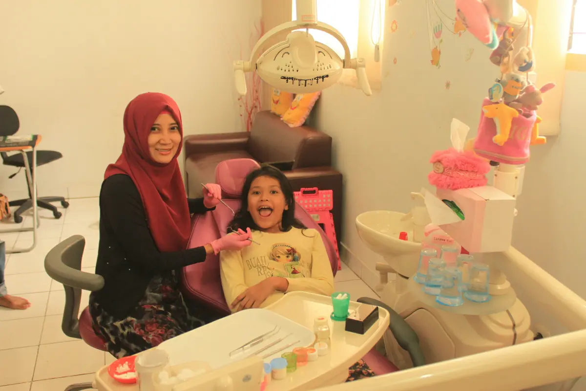 A girl laughing in a dental chair with a grown-up beside her