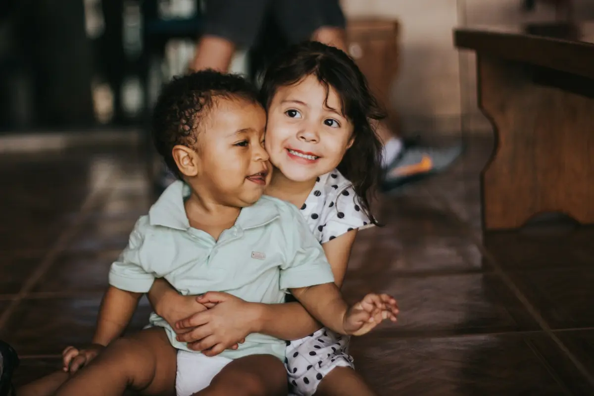 A girl hugging a smiling toddler
