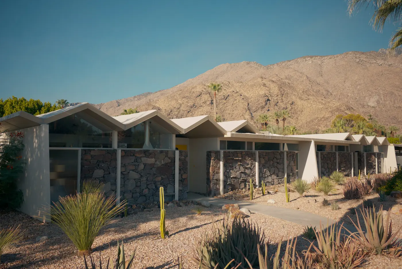 A long house with a folded sawtooth roof in a desert garden