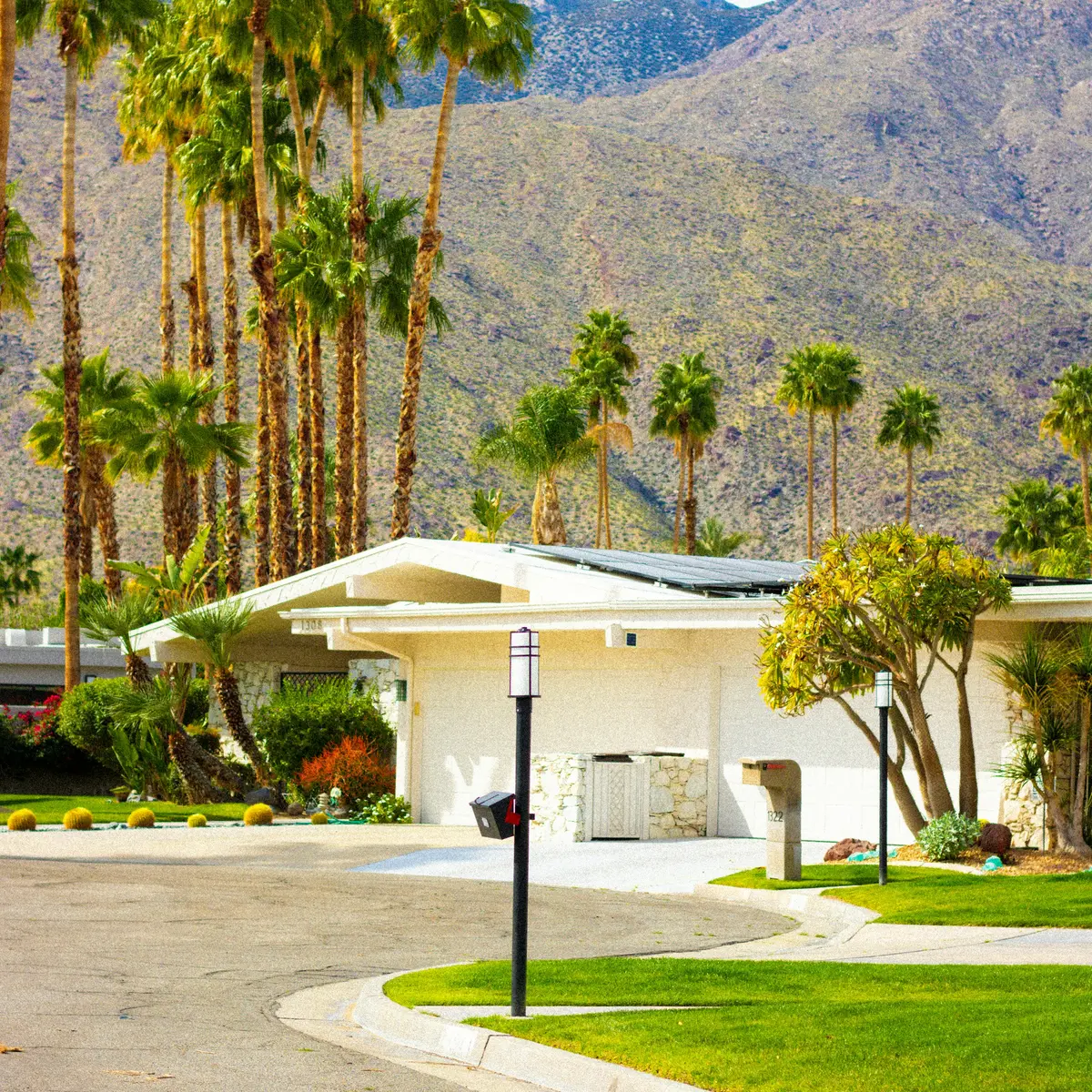 A white mid-century house at the end of a curved drive with the mountain behind