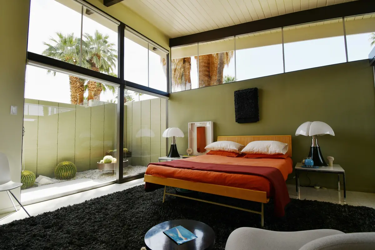 A bedroom with a glass wall onto a private garden