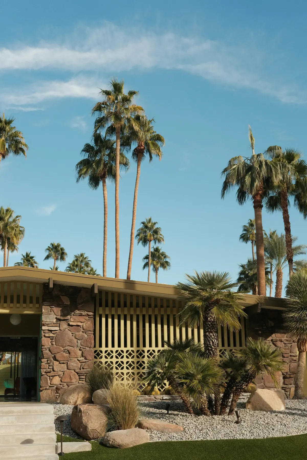A low house with a stone wall and a wooden screen under tall palms