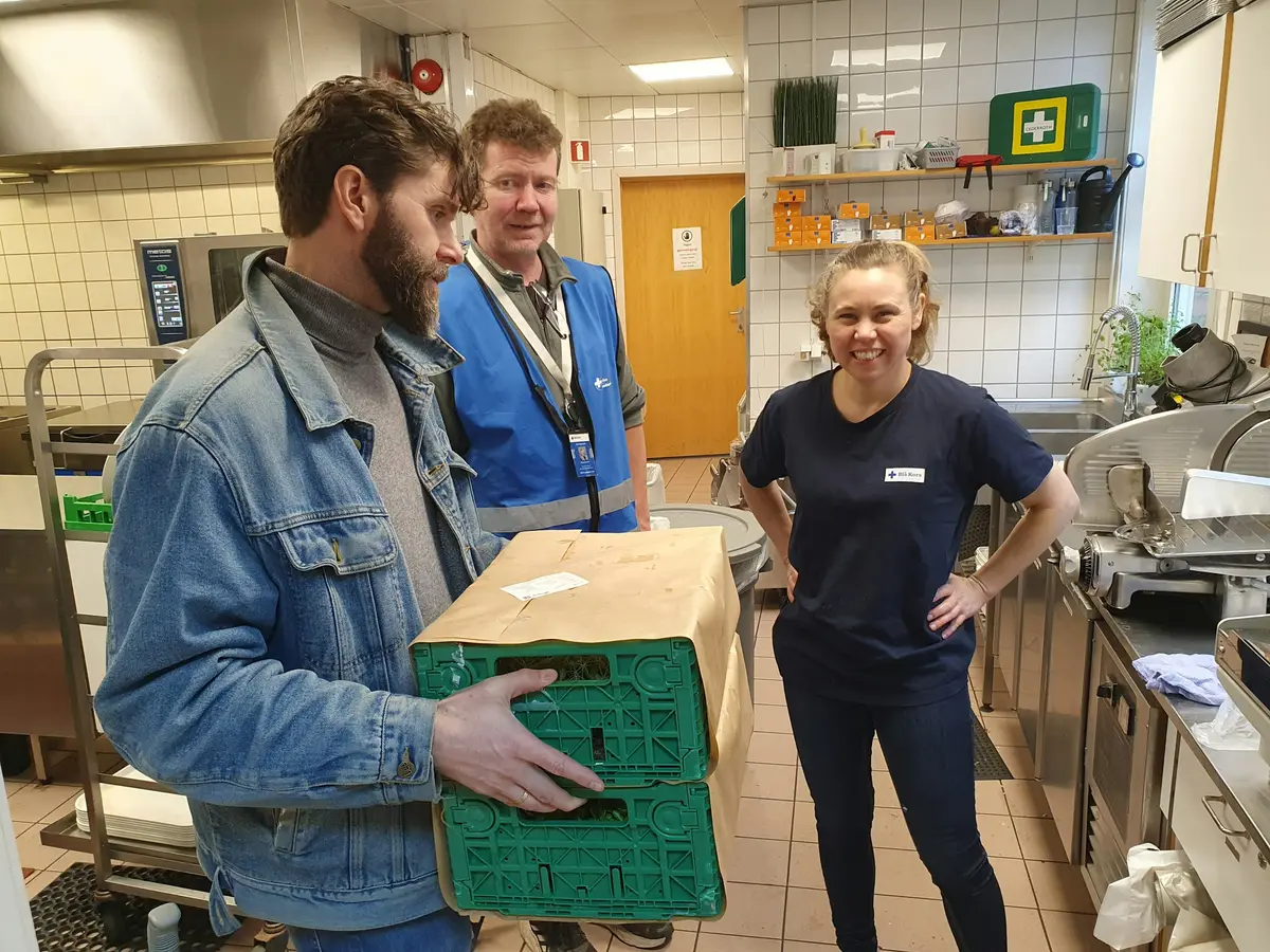 Three volunteers in a kitchen, one carrying a crate of food