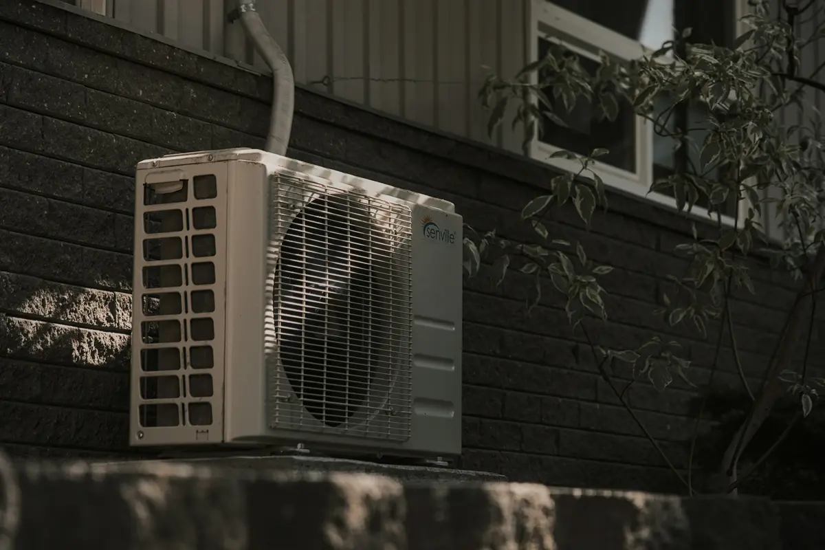 A heat pump outdoor unit on a dark brick wall