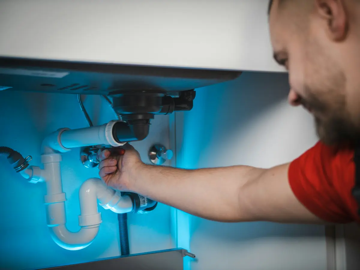 A smiling plumber in a red shirt working on the pipes under a sink