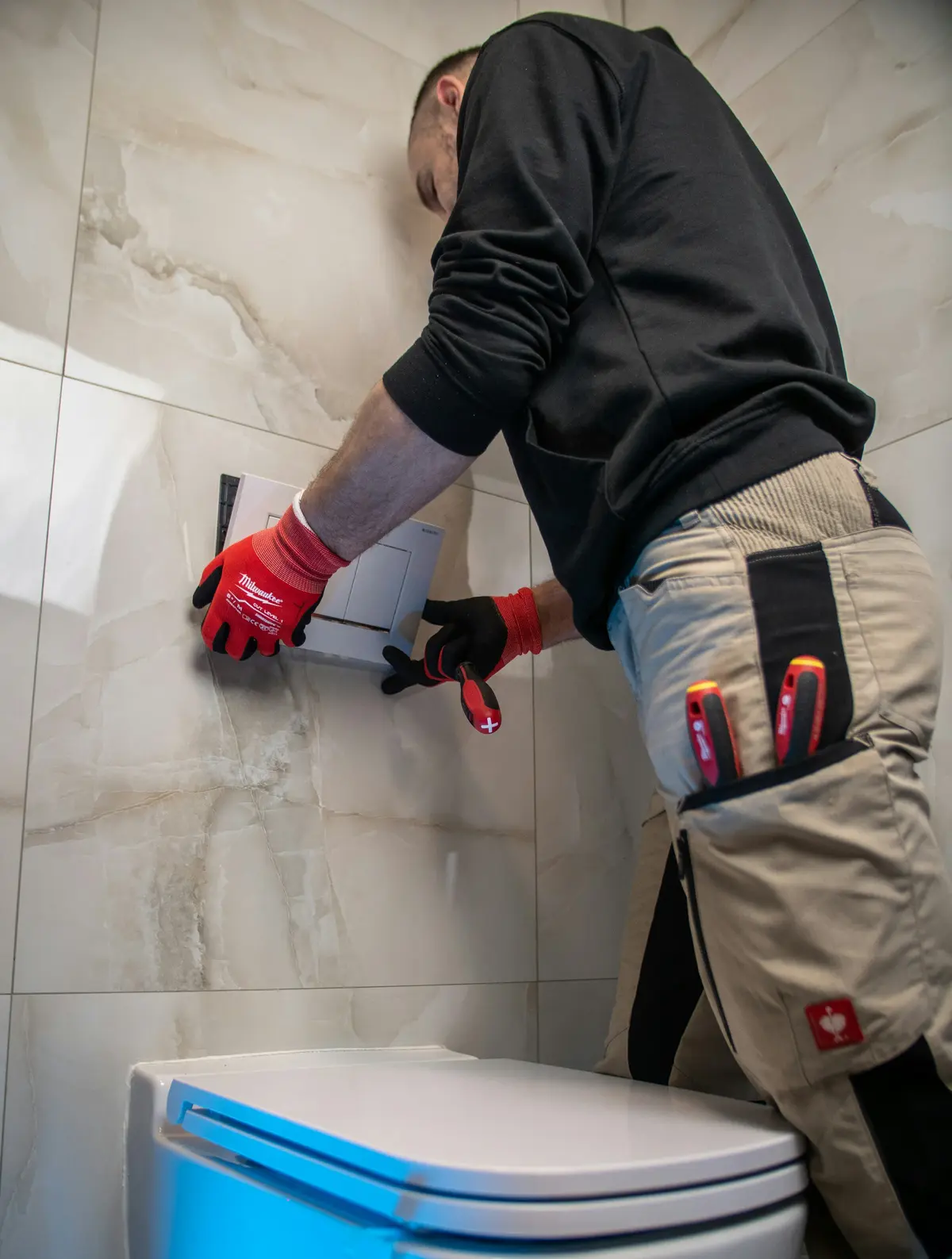 A plumber in work gloves fixing a pipe in a bathroom wall