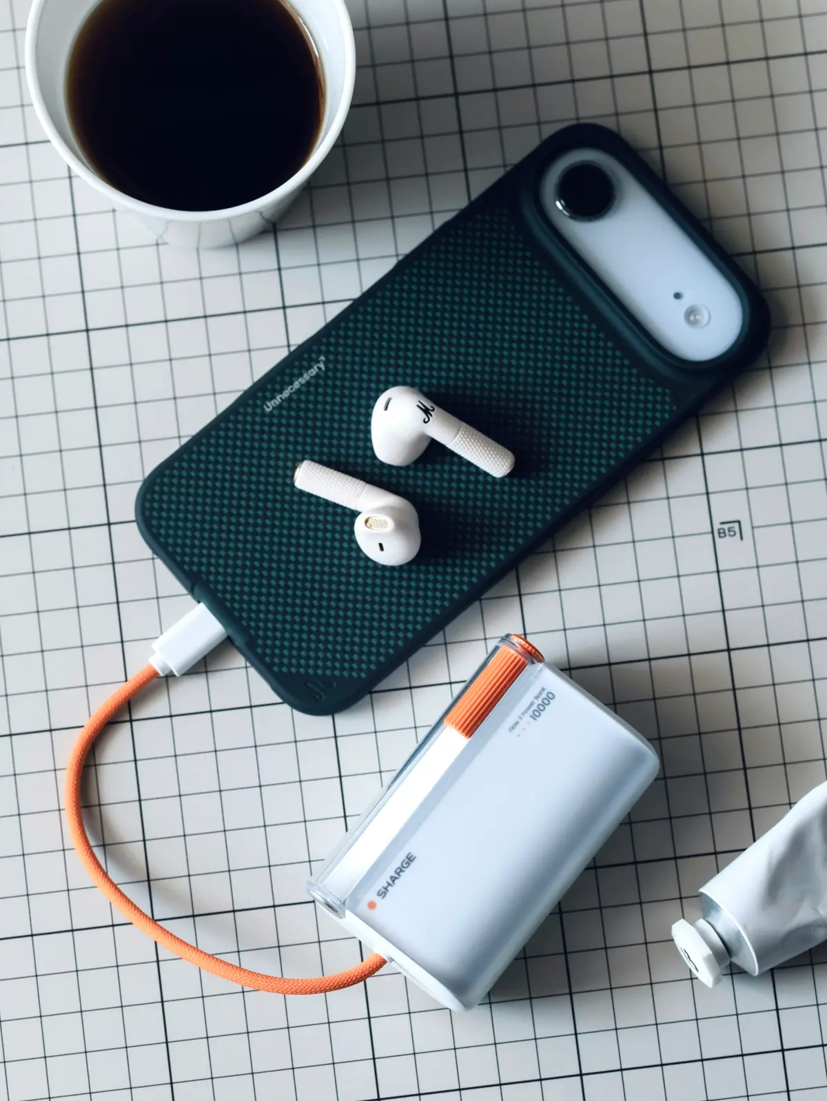 A phone, earbuds, a power bank and an orange cable laid out on a grid mat