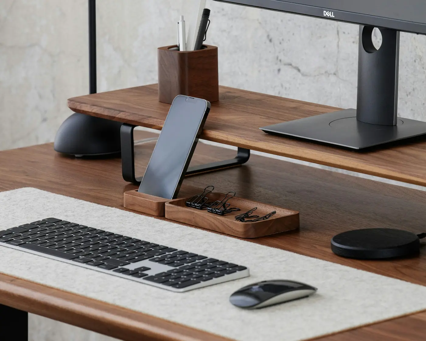 A walnut desk with a monitor, keyboard and a phone on a stand
