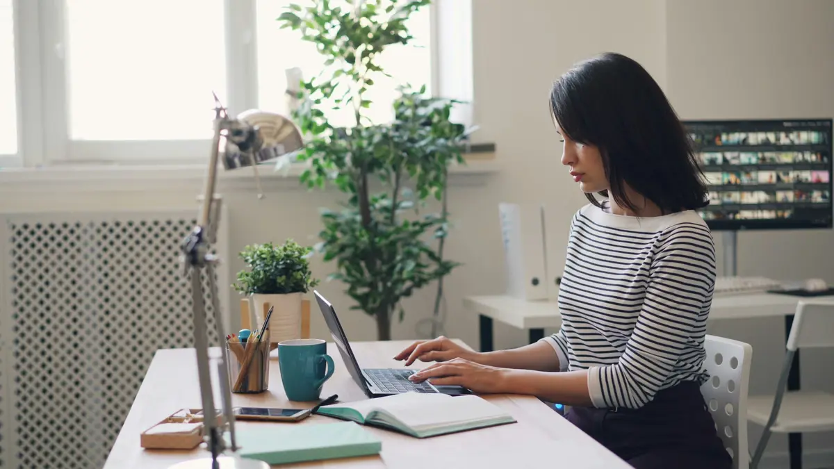 A woman working on a laptop at a white desk in a bright office