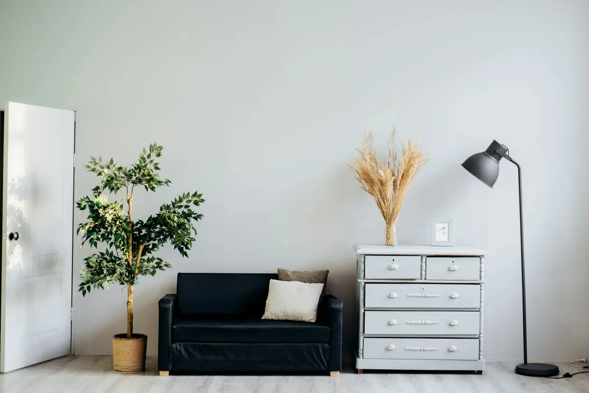 A small black sofa under an empty grey wall, with a dresser and a floor lamp