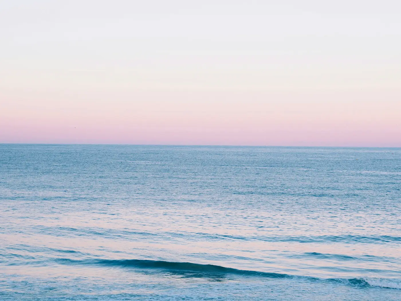 A calm sea at dusk under a pink sky
