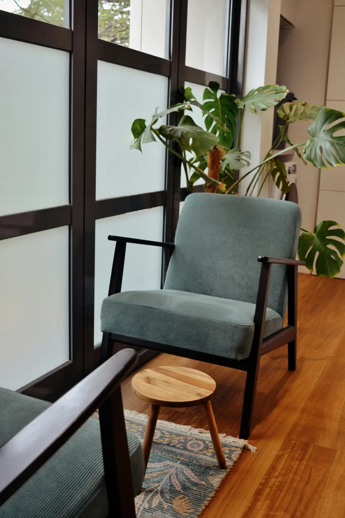 A green armchair by a tall window with plants