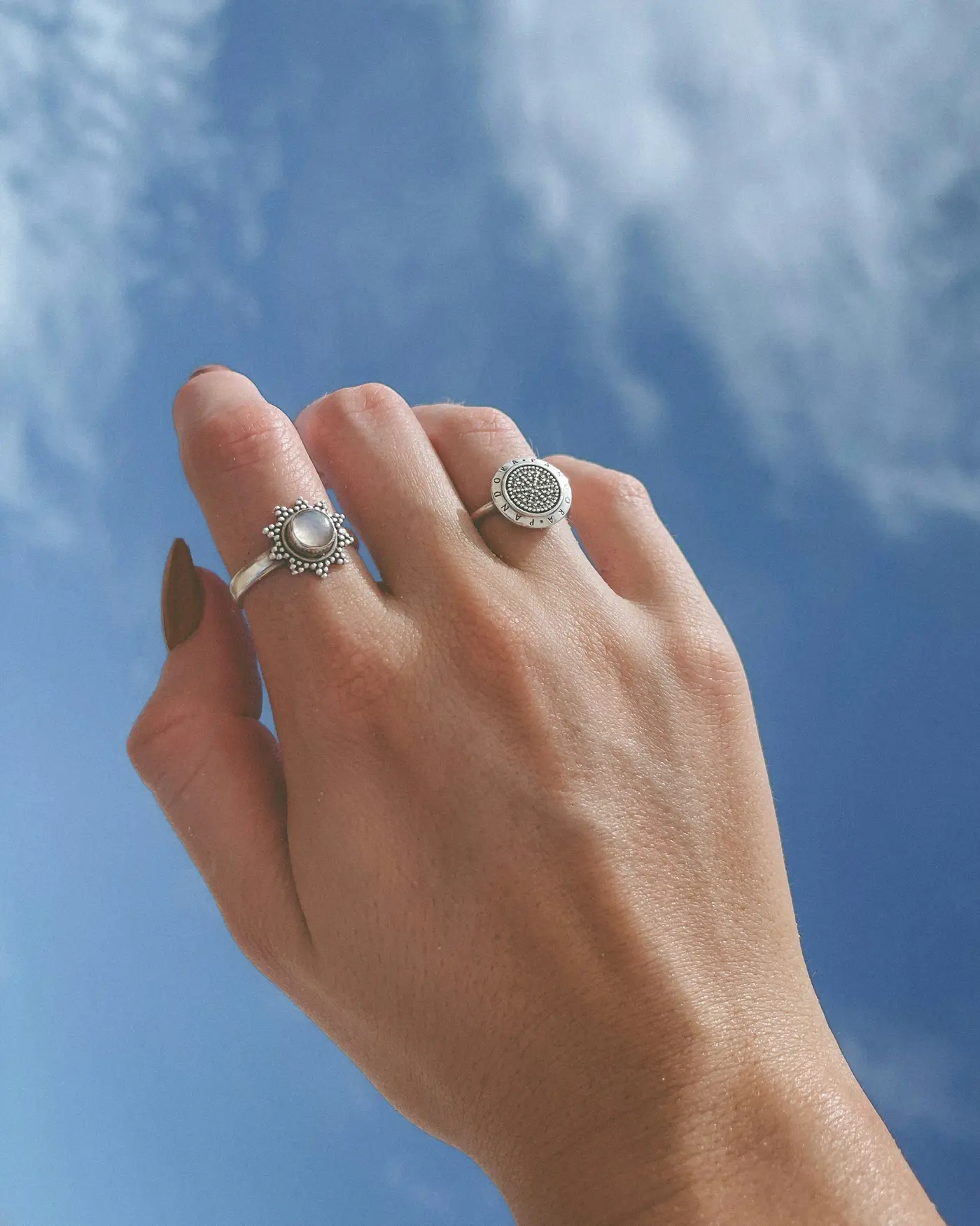 A hand held up against a blue sky, wearing two silver rings