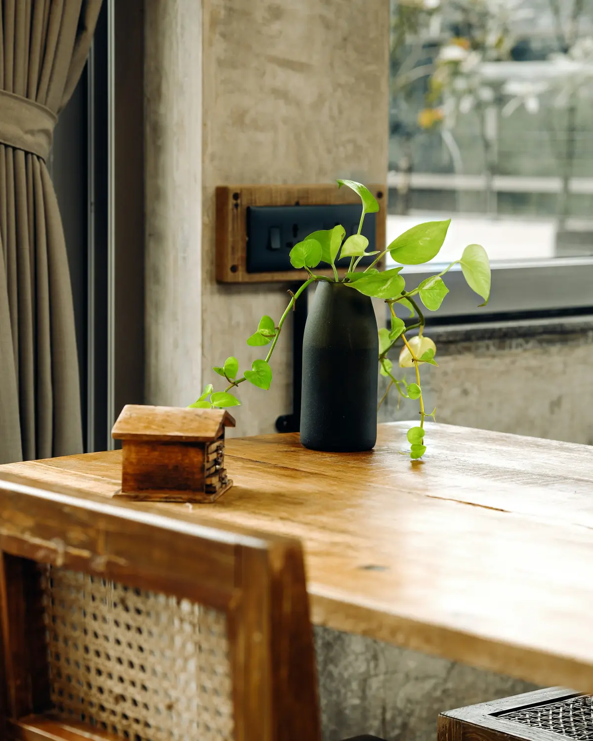 A solid wood table and cane chair by a window with a plant in a vase