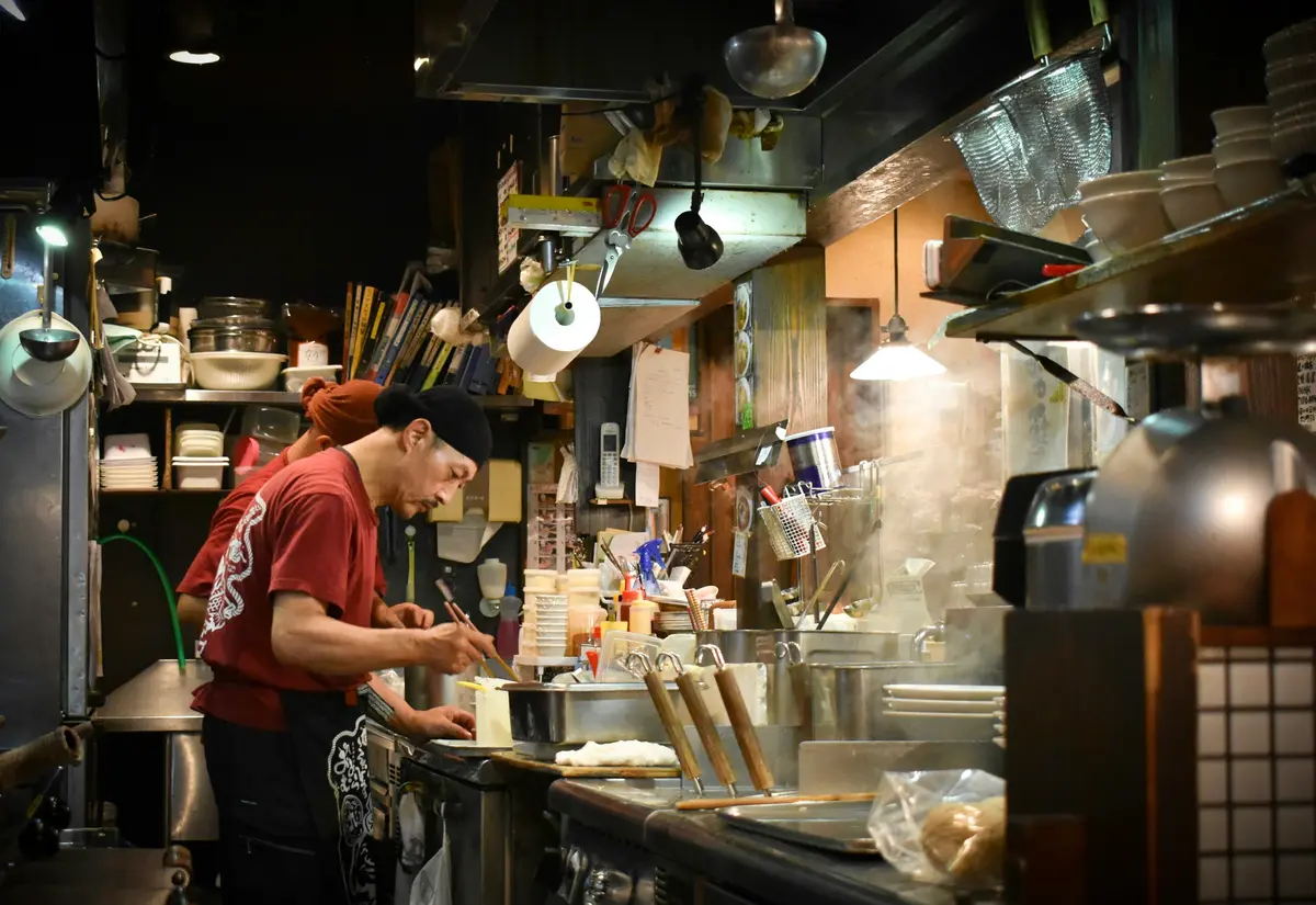 A cook in a red shirt working over steaming pots