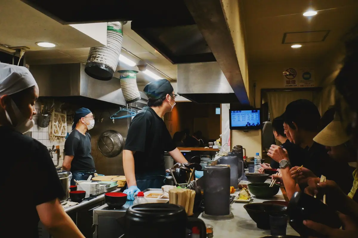 Cooks working a busy ramen counter while people eat