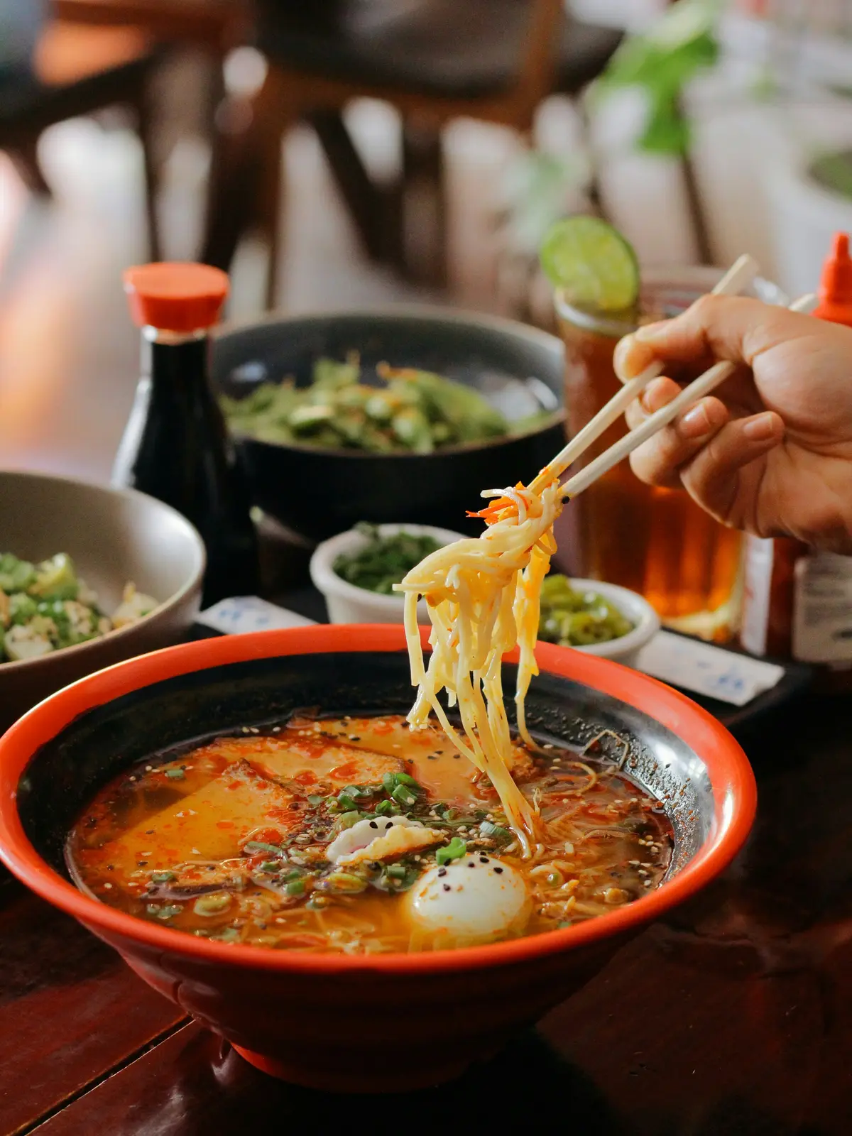 Chopsticks lifting noodles from a red miso ramen