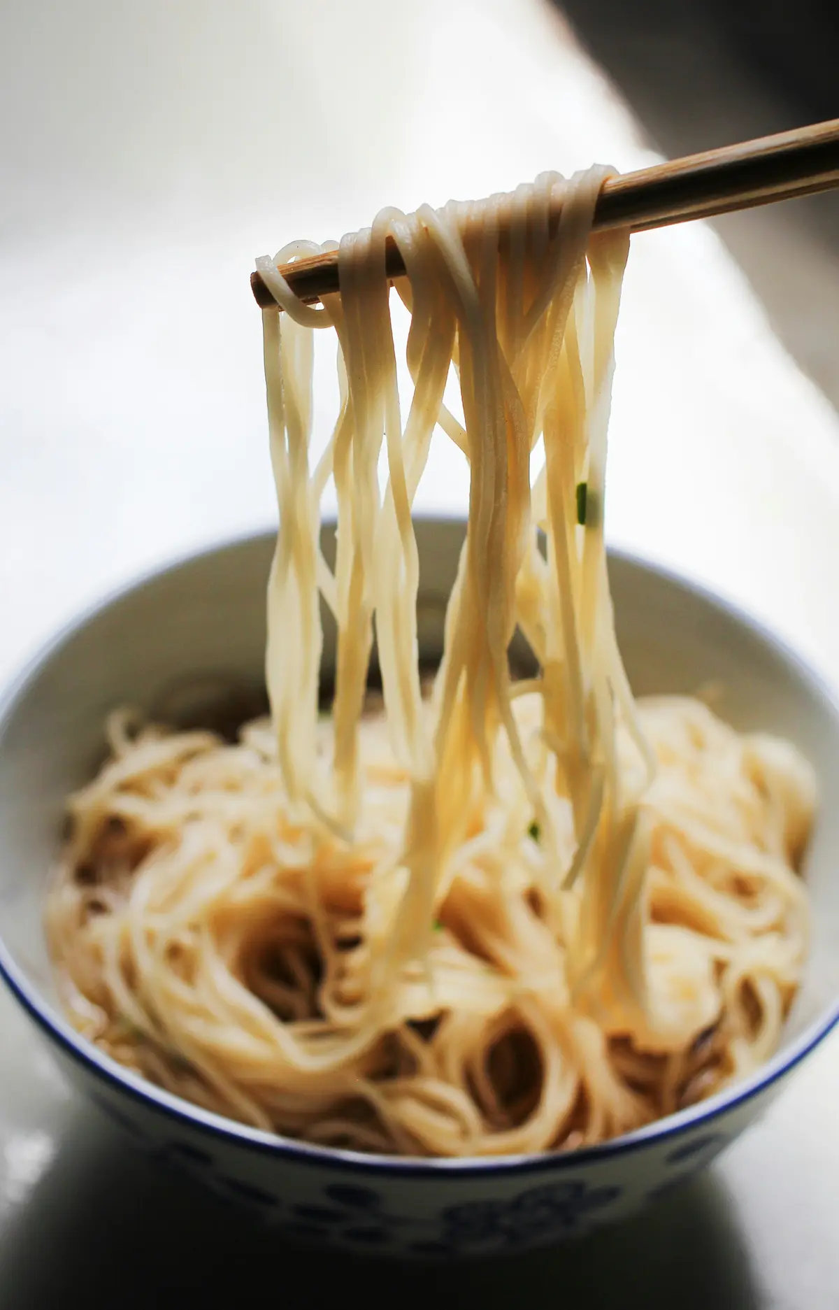 Chopsticks lifting noodles out of a white bowl