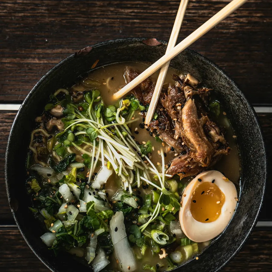 Ramen with greens, pork and an egg, seen from above with chopsticks