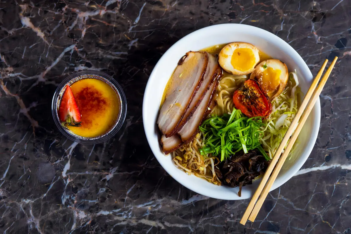 A shio ramen with chashu and soft eggs on a dark marble table