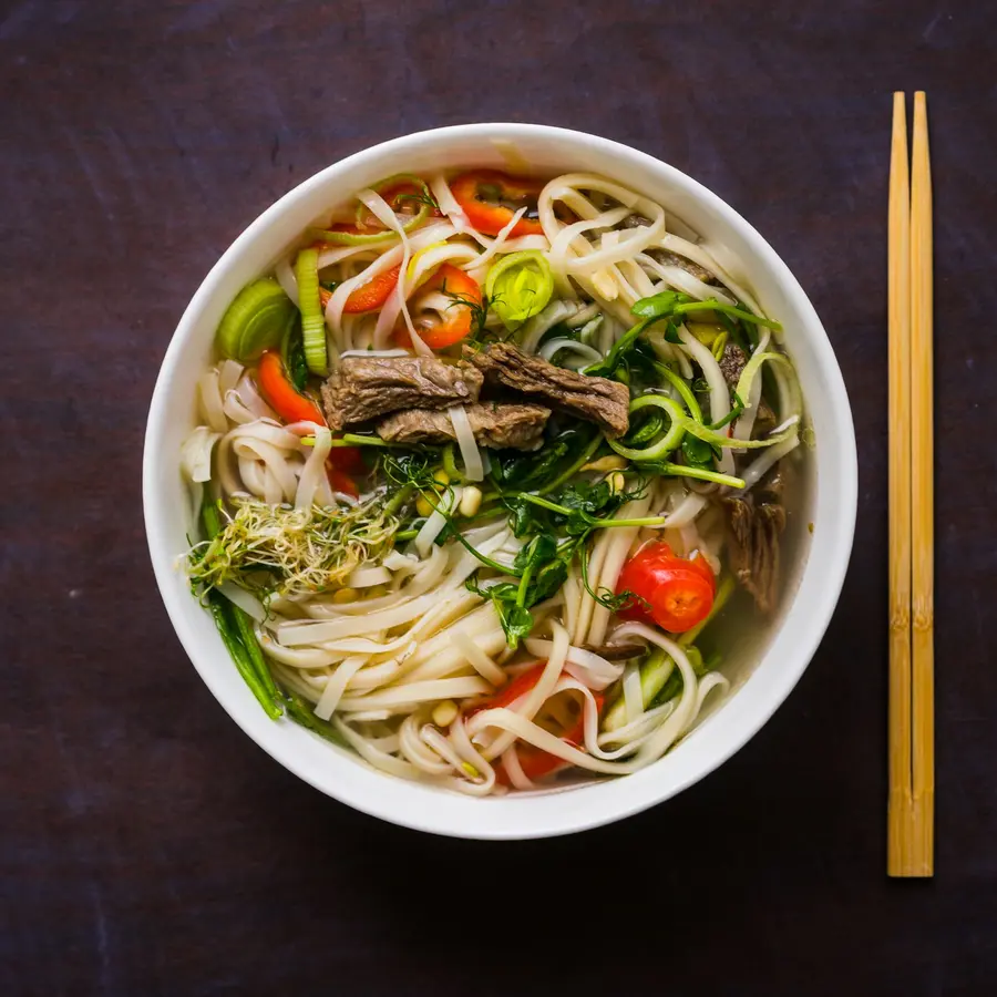A vegetable ramen with seared mushrooms, peppers and greens, chopsticks beside it