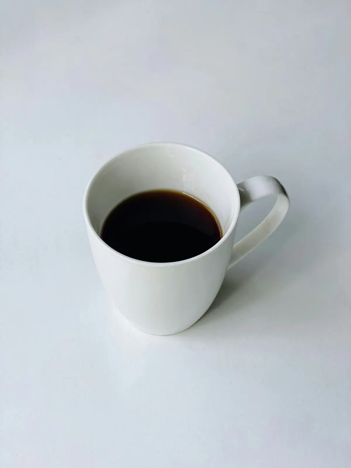 A white mug of black coffee on a white table