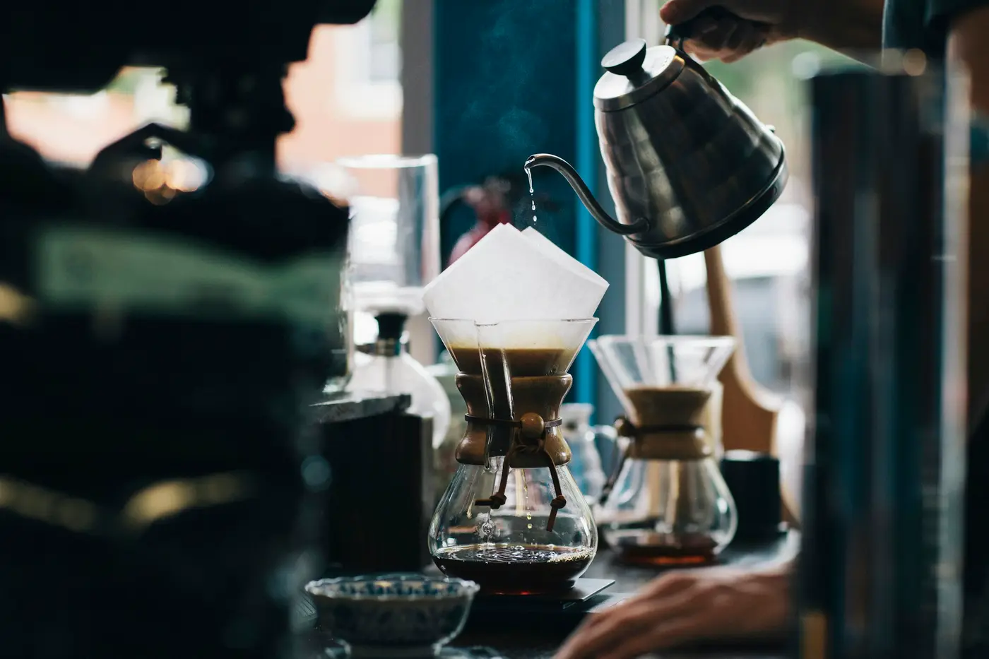 A kettle pouring water over pour-over cones on a coffee bar