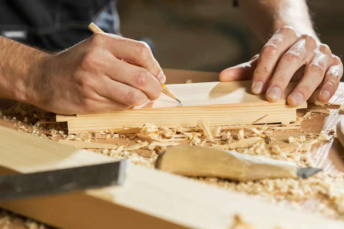 A carpenter marks a cut line on a board with a pencil