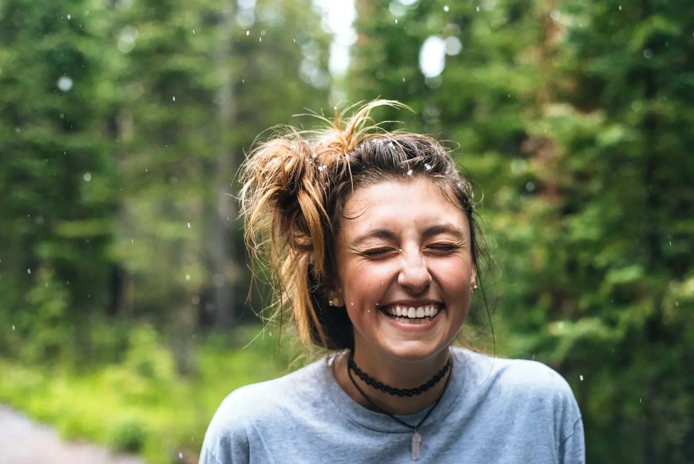 A woman laughing outdoors among green trees