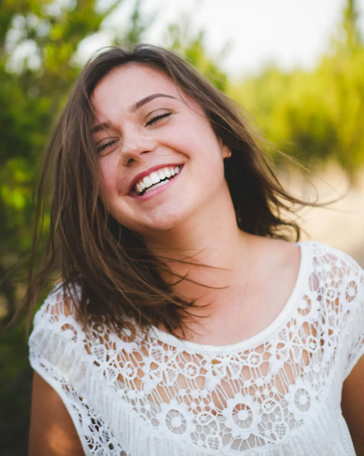 A young woman with long dark hair laughing outdoors